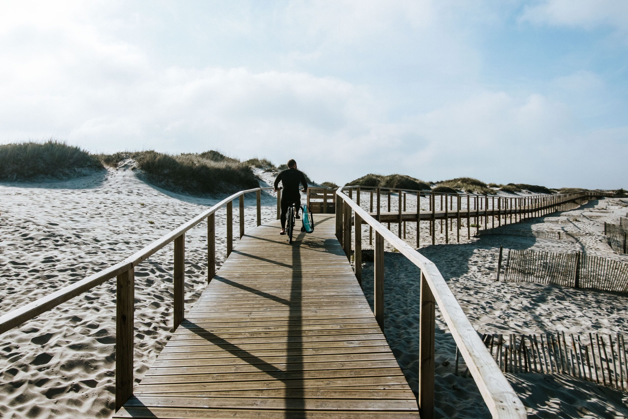 Cycliste poussant son vélo sur un ponton en bois à travers les dunes de La Faute-sur-Mer